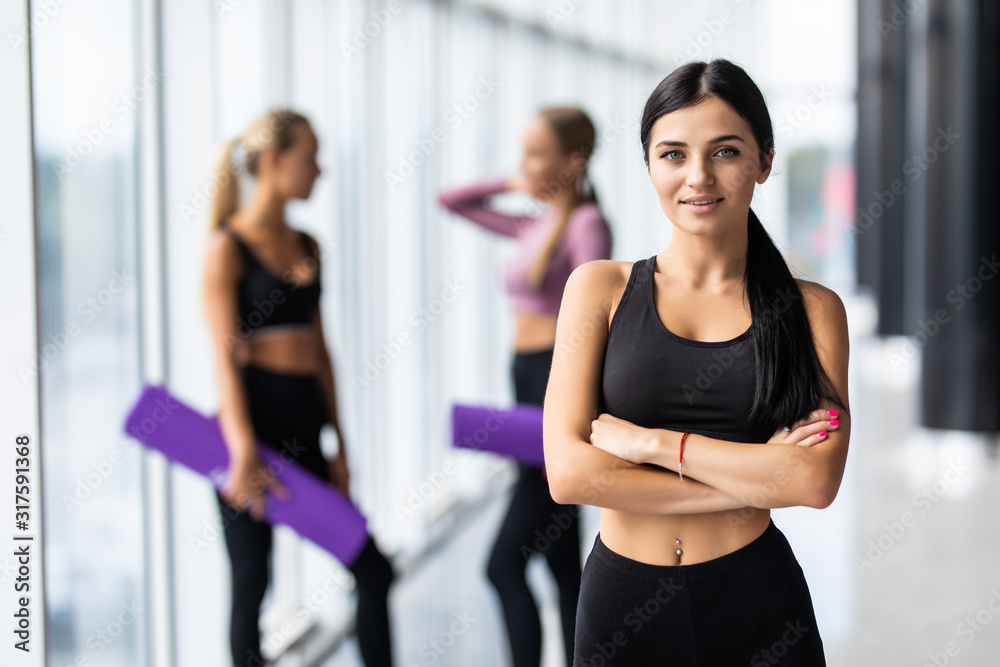 Sport fit woman with perfect body after training standing in front of two fit girls at gym