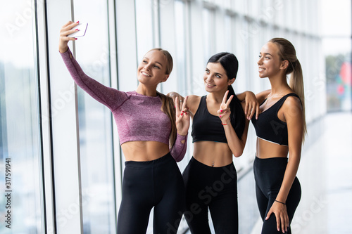 Selfie time, girls. Three girlfriends in fashionable sport outfits are posing for a selfie photo at gym © F8  \ Suport Ukraine