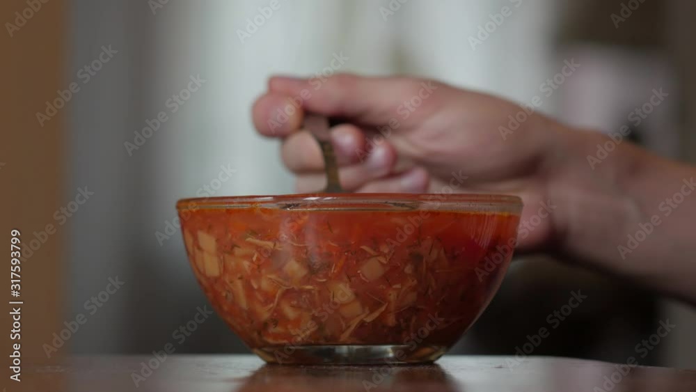 Man eating red soup male hand eats borscht with a spoon from a transparent plate closeup Man eating red soup male hand eats borscht with a spoon from a transparent plate closeup