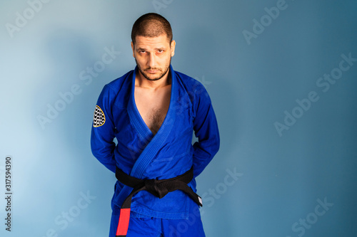 Brazilian jiu jitsu bjj caucasian athlete instructor professor or fighter standing in front of the blue wall wearing kimono gi uniform and black belt looking to the camera photo