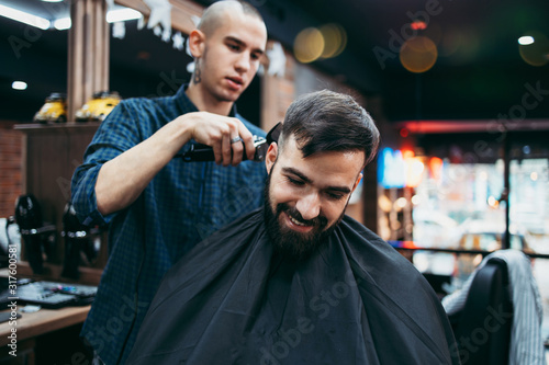 Good looking young adult man getting a hair and beard styling and dressing treatment by professional hairstylist.