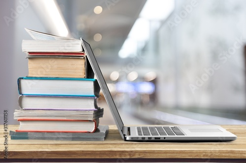 Stack of books with laptop on wooden table photo