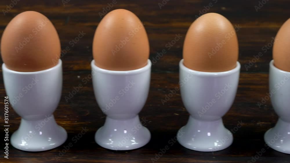 Panning shot along a row of boiled eggs in egg cups on a wooden table to toast soldier being dipped in the yolk of a broken open egg Panning shot along a row of boiled eggs in egg cups on a wooden table to toast soldier being dipped in the yolk of a broken open egg