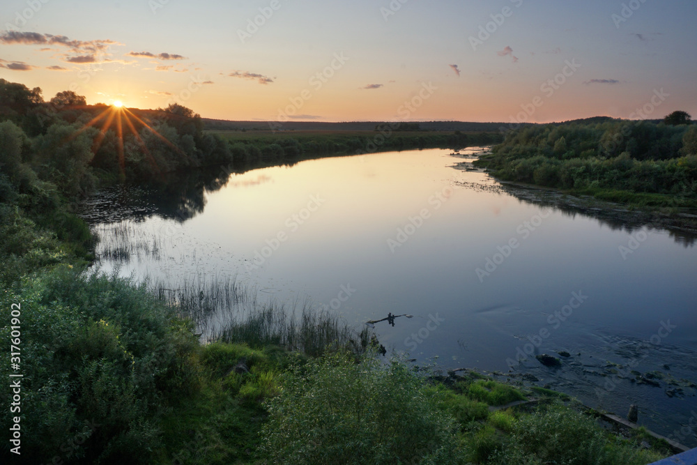 Landscape. Nature. Sunset over a river in a flat ground. Evening, soft lights, green meadows, calm water. The river makes a turn