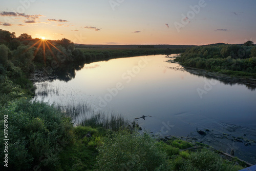 Landscape. Nature. Sunset over a river in a flat ground. Evening  soft lights  green meadows  calm water. The river makes a turn