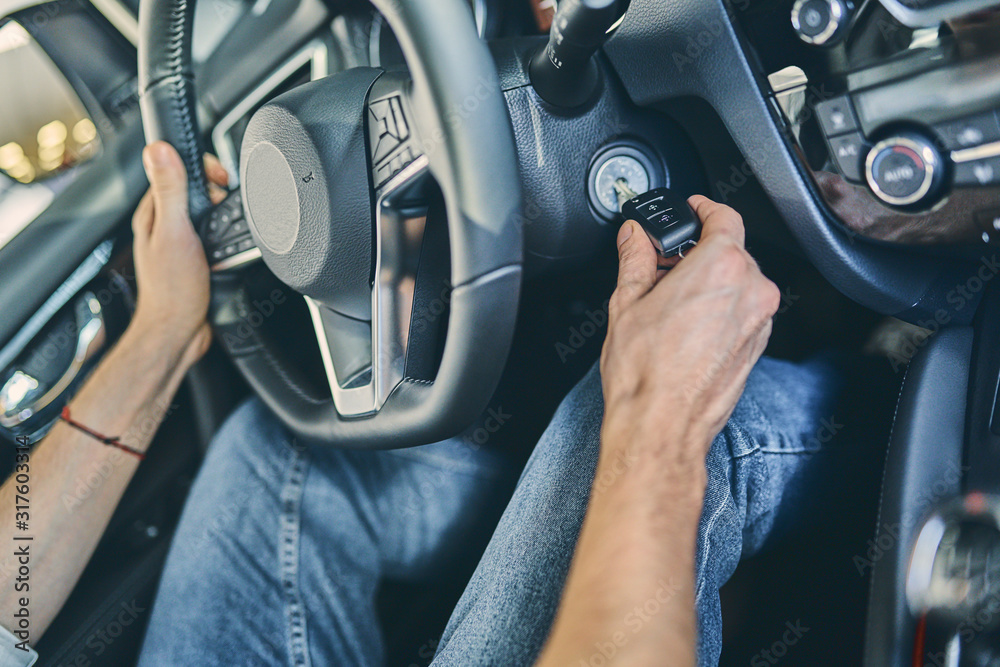 Male hand holding a steering wheel before purchasing a new automobile in showroom.