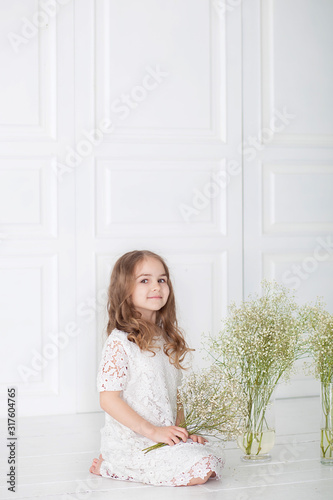 Beautiful little girl with a bouquet of Gypsophila (Baby-breathon). Portrait girl with blond hair in a white dress holding a flowers. Cute baby with a bouquet in hands. On March 8,  Mother's Day