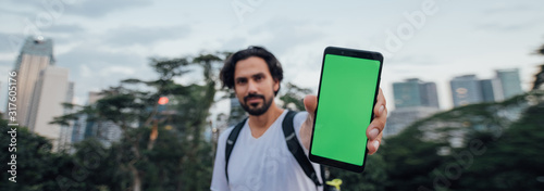 A man holds a phone with a green screen and stands against the backdrop of a metropolis photo