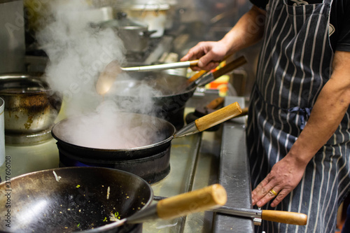 Chefs at work in a commercial kitchen. Male chef cooking using wok styled pans in a takeaway / restaurant setting