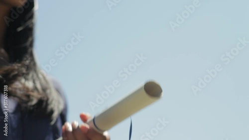 Confident young Indian woman wearing her high school graduation cap and gown receives her diploma and shakes the principal's hand  