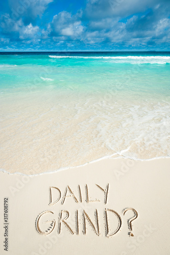 A humorous winter travel message  DAILY GRIND   handwritten on the smooth sand of a tropical island beach