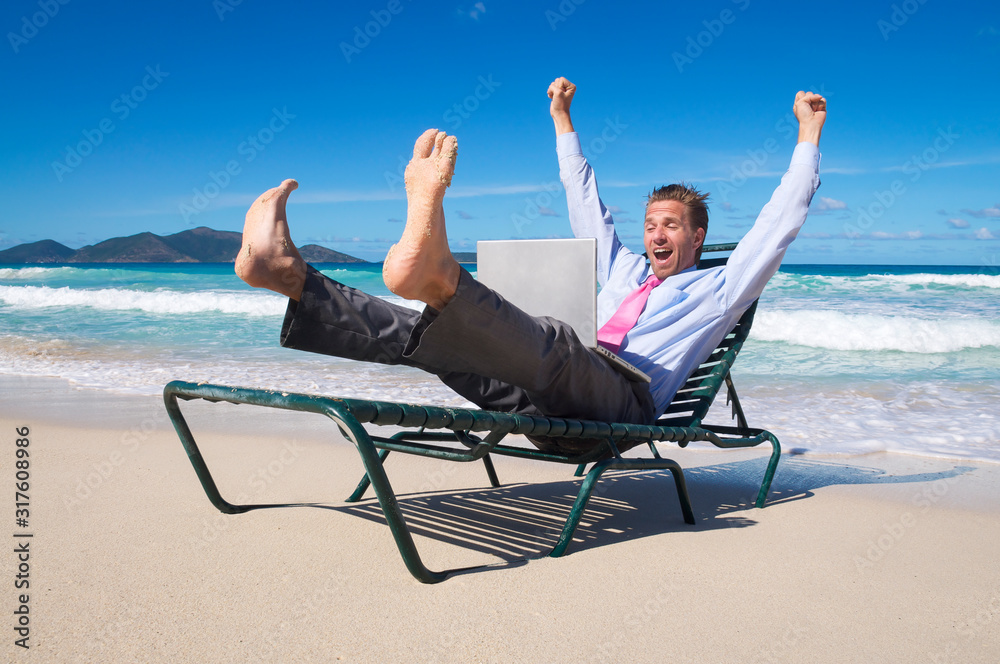 Excited businessman kicking up his bare feet and throwing out his hands as he celebrating with his laptop on a beach chair