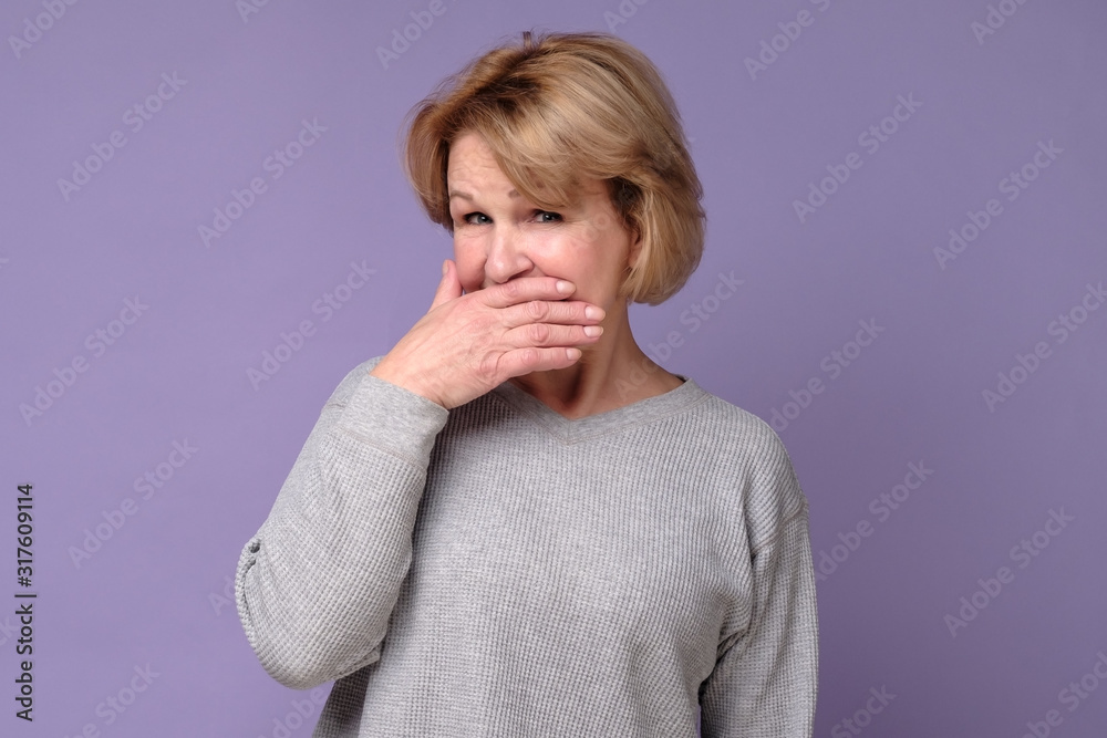 Senior older woman with puzzled look covering her mouth trying to keep secret. Studio shot Senior older woman with puzzled look covering her mouth trying to keep secret. Studio shot