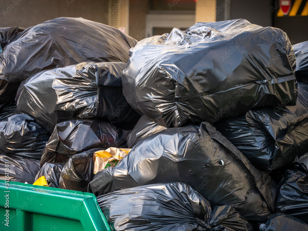 A lot of black plastic bags of garbage are dumped in a dumpster A lot of black plastic bags of garbage are dumped in a dumpster