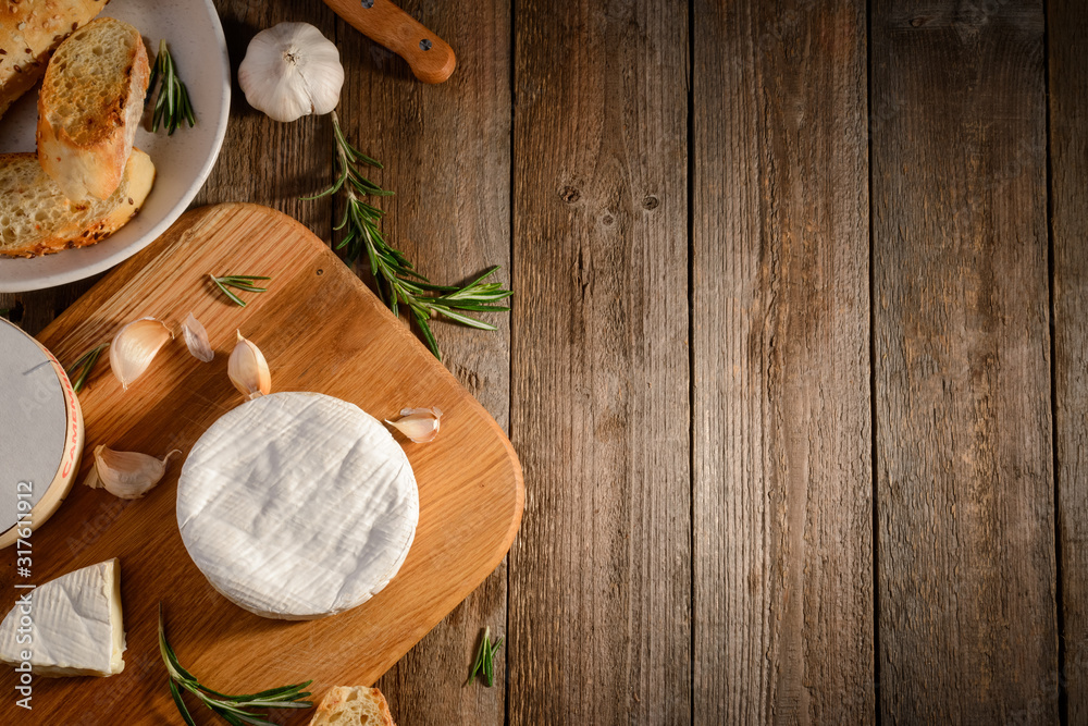 Camembert cheese, garlic, bread and rosemary on a rustic wooden table