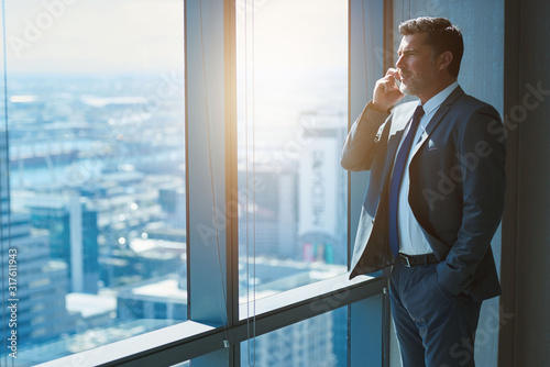 Mature business CEO talking on phone alongside large high windows photo