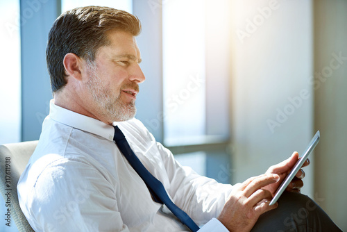 Mature businessman looking positive and using digital tablet