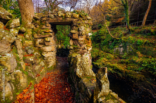 Stone gate of old pathway with river below and green mossy rocks in Tollymore Forest Park in autumn, Newcastle, County Down, Northern Ireland © Dawid
