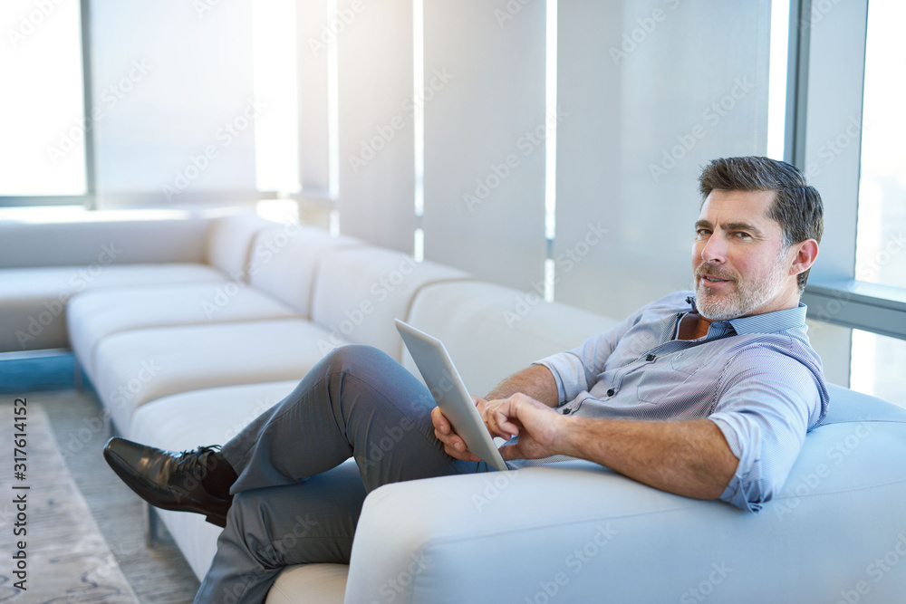 Stylish mature businessman smiling on couch with a digital tablet
