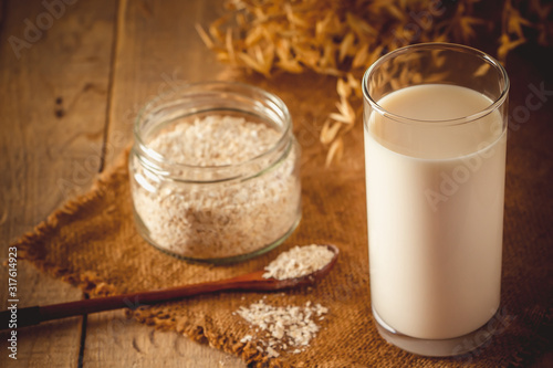 Glass of oat milk on a wooden background. Lactose-free vegetable diet milk. Gluten free oat drink on a brown wooden background.