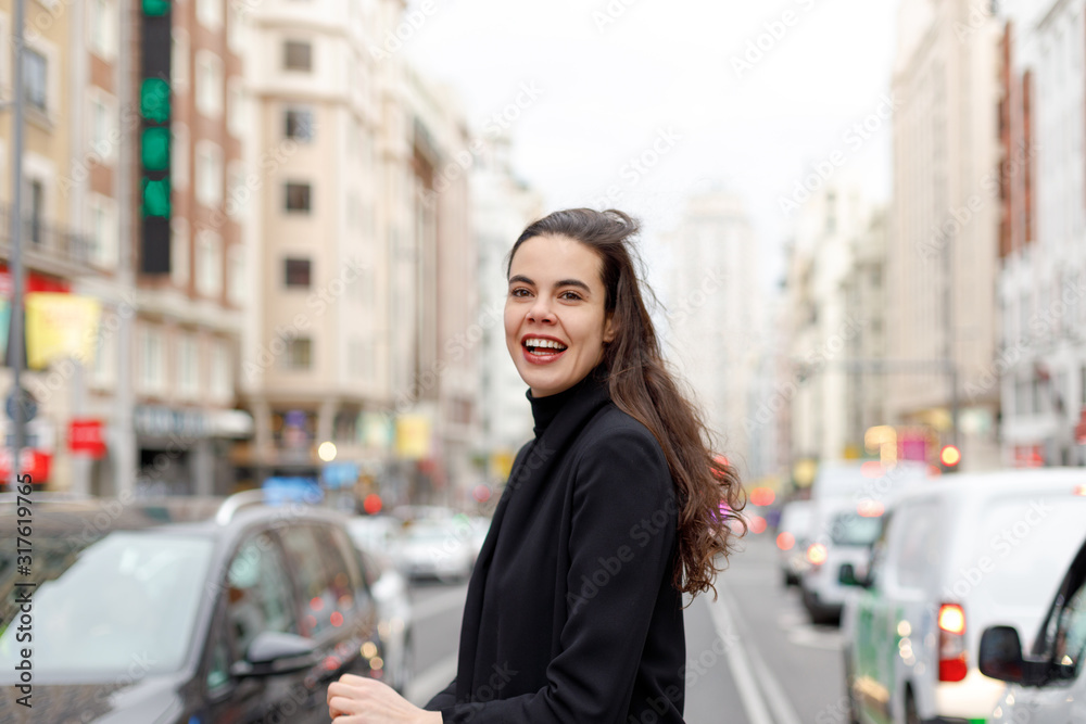 Smiling woman in a black jacket suit crossing the downtown street