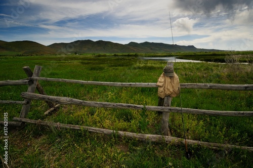 A fly fisherman's geart rests against a rustic wood fence at Silver Creek, Idaho, USA