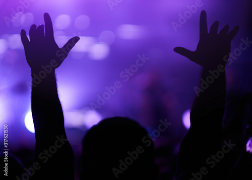 Audience with hands raised at a music festival and lights streaming down from above the stage. Crowd raising their hands, dancing and enjoying great the concert.
