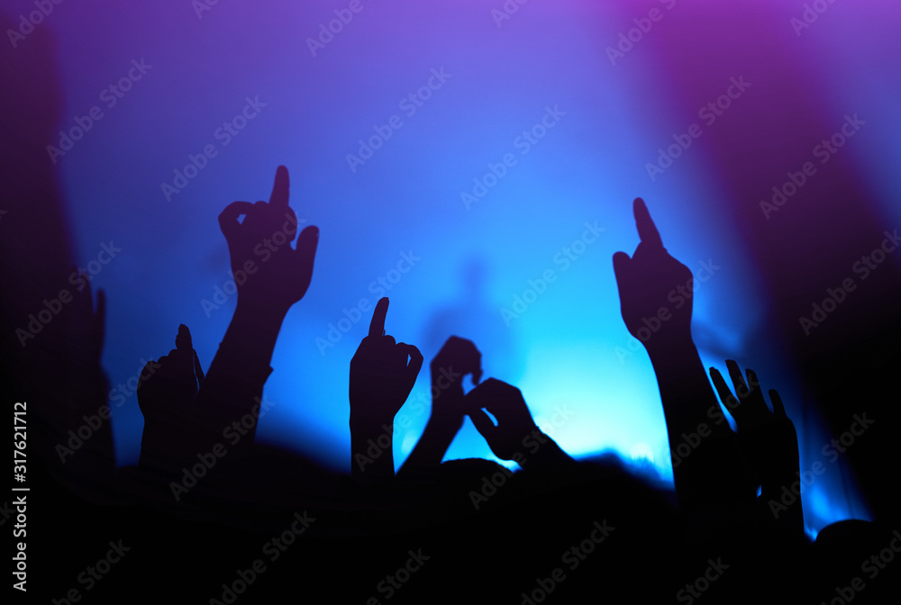 Audience with hands raised at a music festival and lights streaming down from above the stage. Crowd raising their hands, dancing and enjoying great the concert.