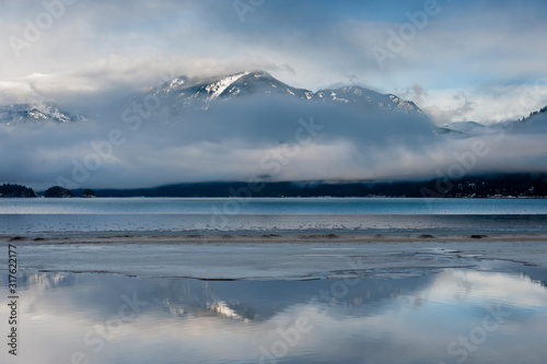 Harrison Lake, British Columbia, Canada in Winter. Low clouds envelope the surrounding mountain range with snow capped peaks seen in the background.