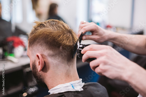 Close up shot of man getting trendy haircut at barber shop. Male hairstylist serving client, making haircut using machine and comb