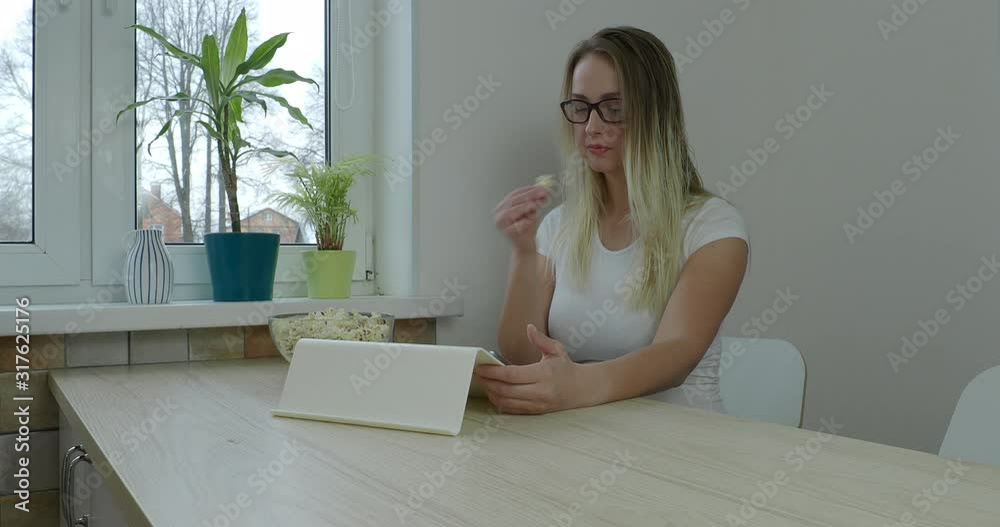 Cute woman looking at the screen her tablet and eating popcorn