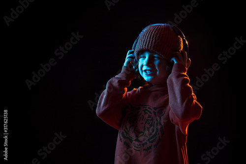 Listening to music and dancing. Caucasian boy's portrait on dark studio background in neon light. Beautiful curly model. Concept of human emotions, facial expression, sales, ad, modern tech, gadgets.