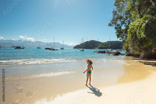 Child playing in the sand at Abraaozinho Beach with taxi boat and blue waters in Abraao, on the tropical Ilha Grande, Angra dos Reis, in the south of Rio de Janeiro Brazil photo