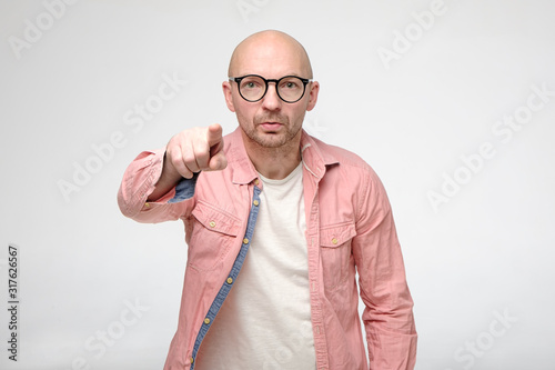 Worried man accuses someone by pointing finger at the guilty person and looks at the camera with a serious look. photo