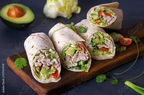 Turkey wraps with avocado, tomatoes and iceberg lettuce on chopping board. Tortilla, burritos, sandwiches, twisted rolls photo