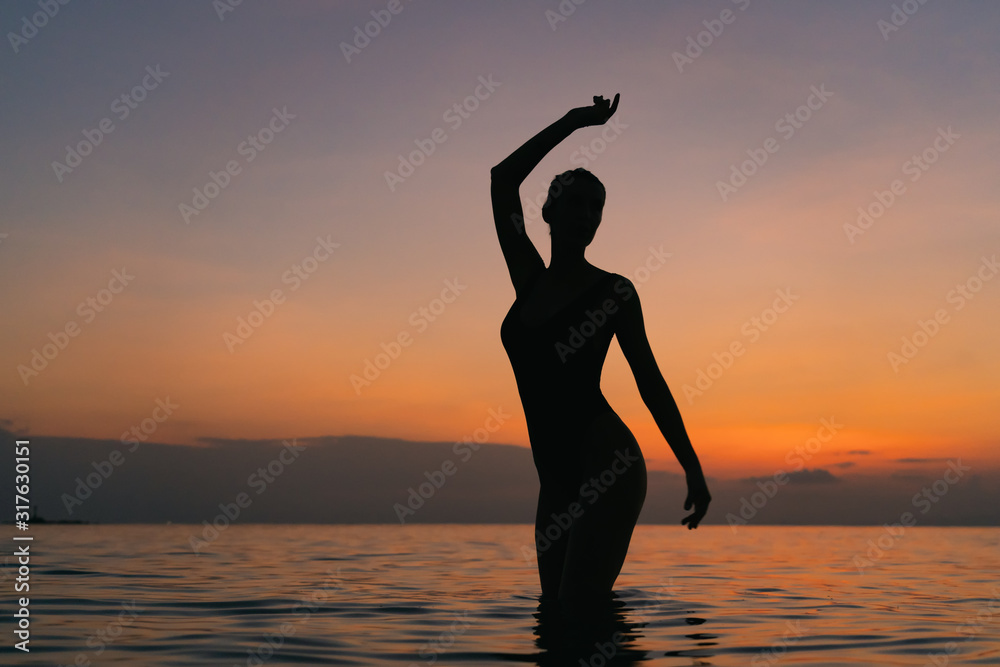 Silhouette of a happiness young slender woman standing in the sea against the background of dawn