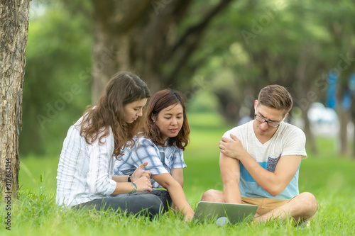 Picture of group of university students multi-ethnic sitting on the green grass working and reading outside together in a park 
