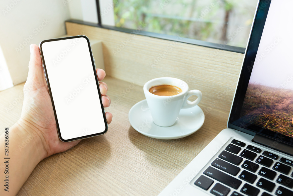 Fototapeta premium Mockup image blank white screen cell phone.man hand holding texting using mobile on desk at coffee shop.background empty space for advertise text.people contact marketing business,technology 