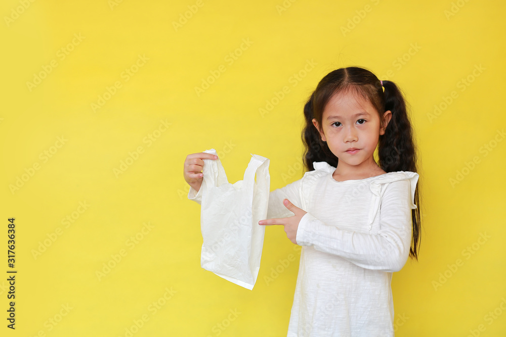 Asian little girl showing a white thin polythene plastic bag isolated on yellow background. Reduce global warming concept.
