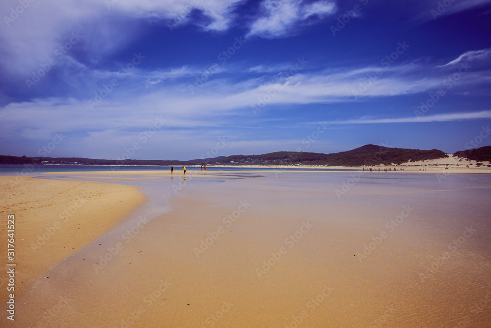 Ocean shore at low tide. Wide sand space. Beach and some people on the horizon. Dark blue sky. Fingal Bay, Australia