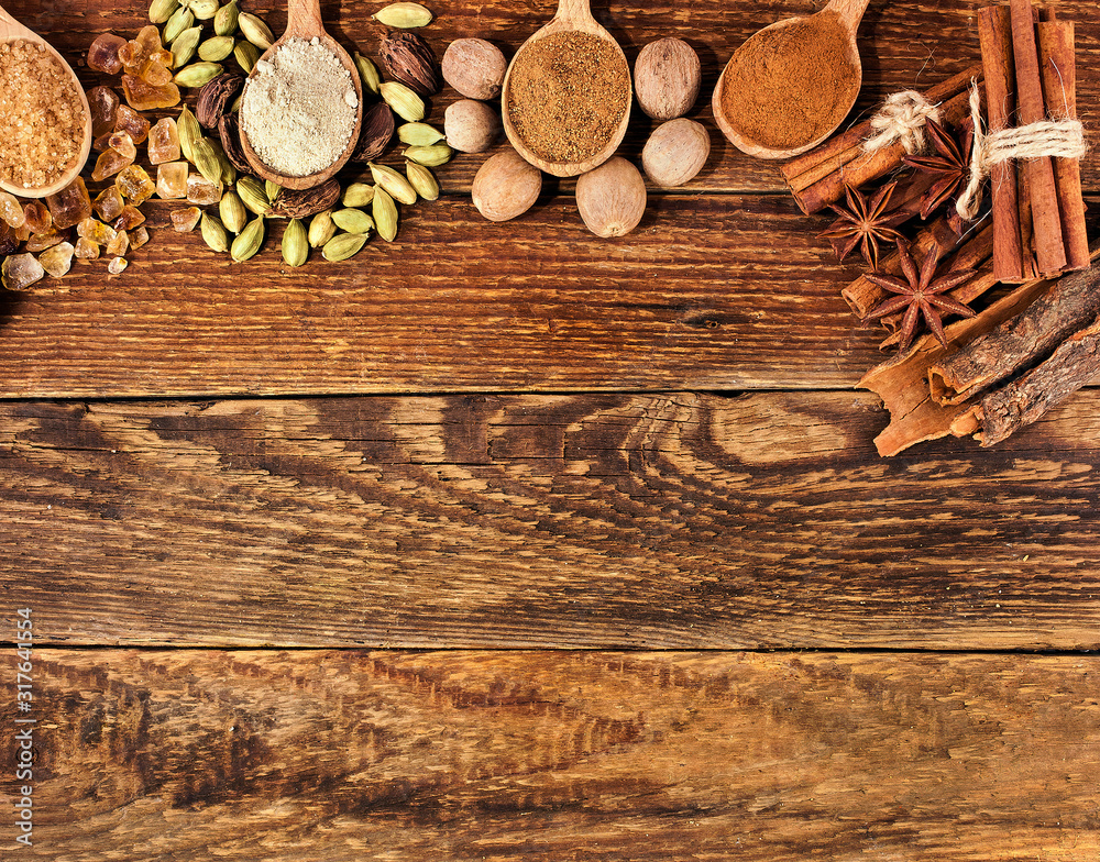 Brown sugar crystals, cardamom, nutmeg, cinnamon sticks, star anise and powder of nutmeg, brown sugar in a wooden spoon on wooden background. Sweet spices. Text space.