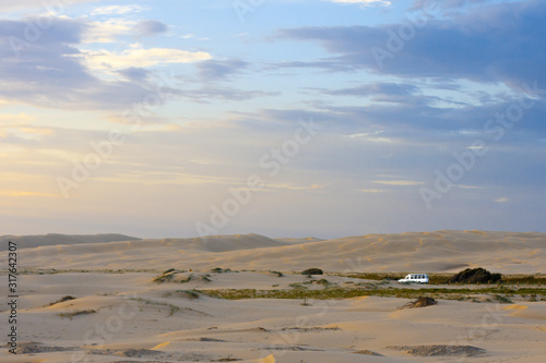 Wide boundless flat desert, soft sunrise light and a point of a white car driving along it far away. Stockton Sand Dunes near the coast, Worimi Regional Park, Anna Bay, Australia photo