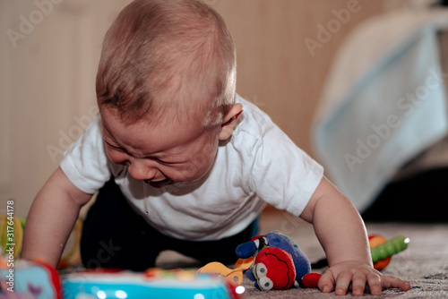 Baby cries on toys. The boy is very upset. The child cries while standing on all fours. The kid blushed with tension.