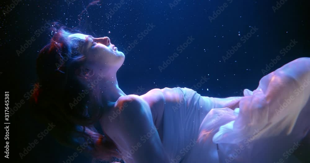 a beautiful girl with long hair is drowning in dark water. she holds up her hands. side view