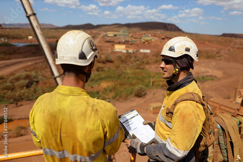 Miner senior businessman supervisor wearing white safety hard hat protection holding folder paperwork and conducting safety checking list on younger newest miner construction mine site Sydney  © Kings Access