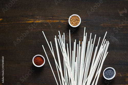 Different kind of spices and raw udon noodles on dark wooden background. Collection of spices coriander poppy sumac and sesame. Asian or Indian food concept.