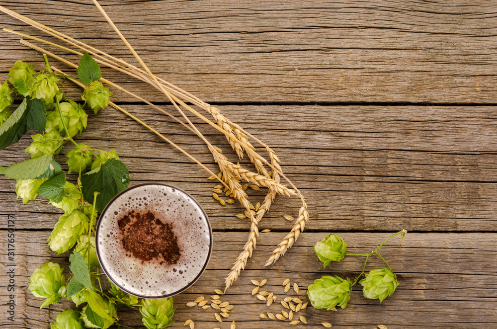 Beer in glass, hops plant green cones, barley and wheat ears on wooden table background, copy space Beer in glass, hops plant green cones, barley and wheat ears on wooden table background, copy space