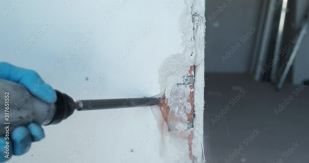 Close-up of white plastered wall, puncher worker begins to break off pieces of brickwork, dust flies, construction debris breaks off, demolition of major wall, deconstruction of interior walls, work Close-up of white plastered wall, puncher worker begins to break off pieces of brickwork, dust flies, construction debris breaks off, demolition of major wall, deconstruction of interior walls, work