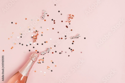 Champagne bottle, confetti stars, holiday and party decoration on pink backgr...