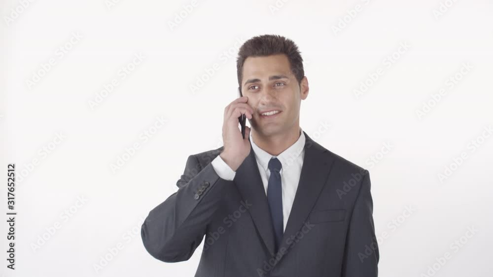 Medium shot of mixed-race good-looking businessman with dark hair and brown eyes chatting on cellphone and laughing against white wall Medium shot of mixed-race good-looking businessman with dark hair and brown eyes chatting on cellphone and laughing against white wall